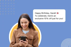 Image of a woman on her phone with a message pop-up next to her showing a special 15% birthday discount offer. An example of personalized outreach via WhatsApp to celebrate a customer's special day.